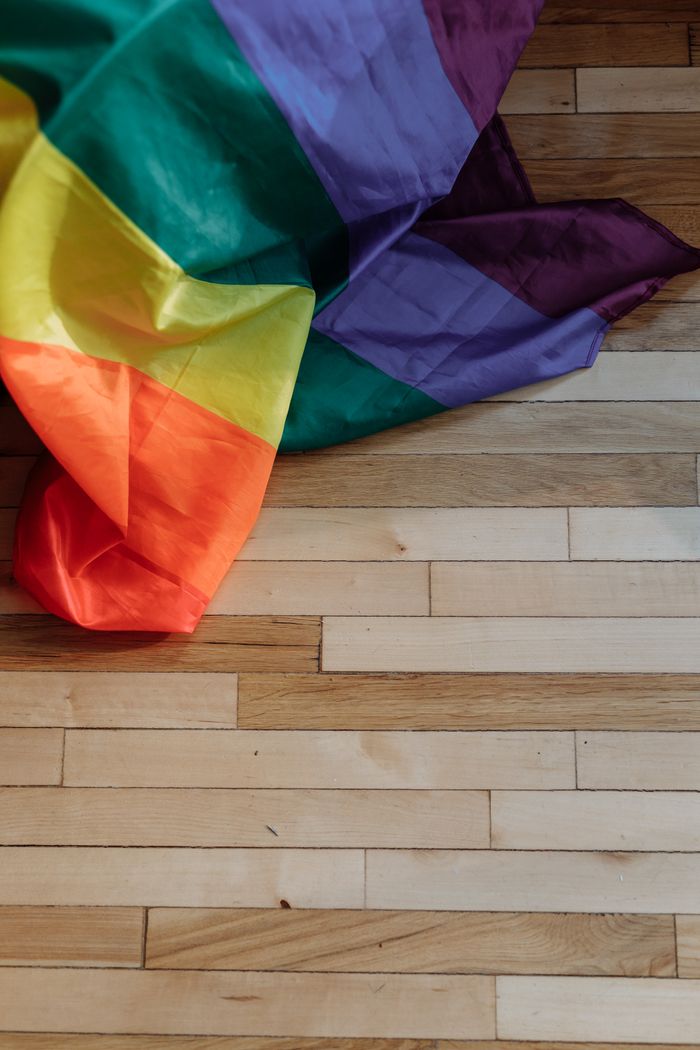 A vibrant rainbow pride flag lays on a wooden floor, symbolizing LGBTQ+ pride and diversity.