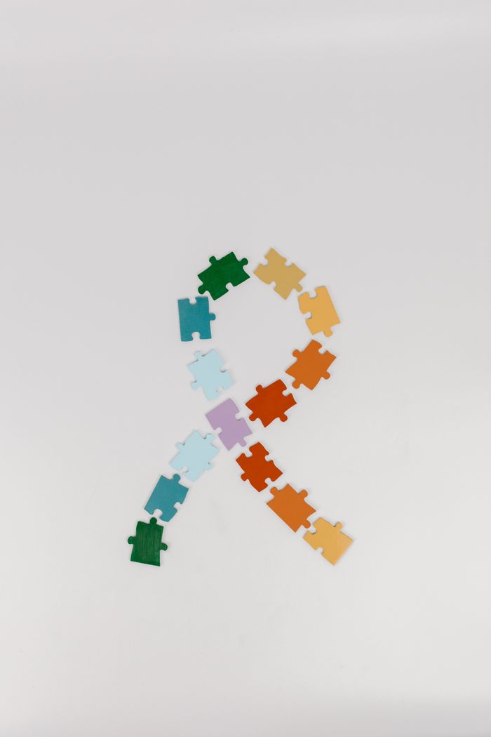 Colorful puzzle pieces arranged in awareness ribbon shape on white background.